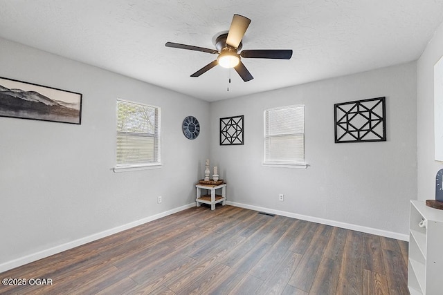 empty room with visible vents, baseboards, ceiling fan, a textured ceiling, and dark wood-type flooring