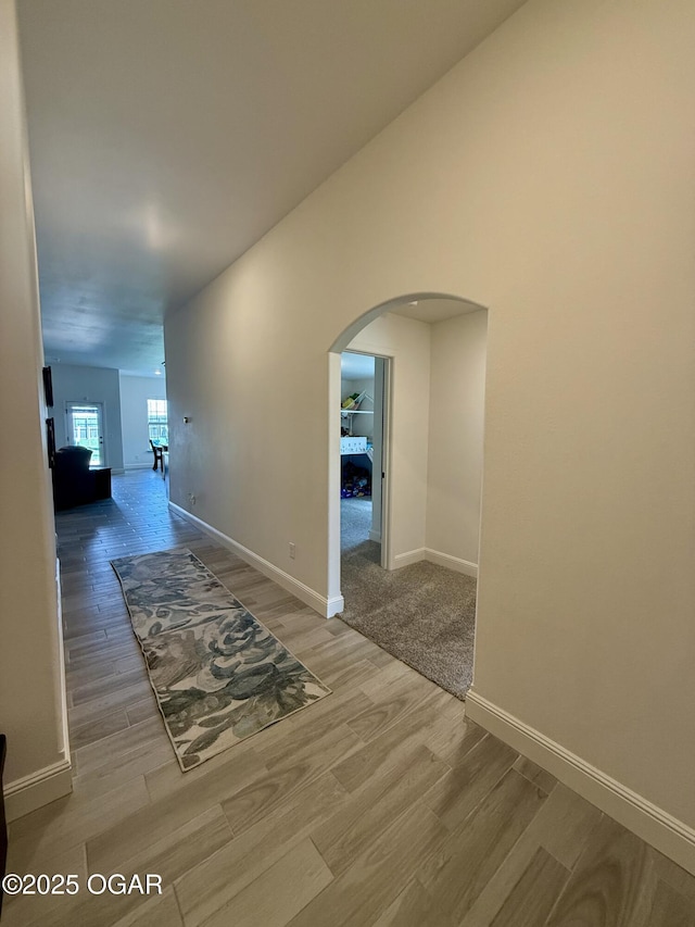 corridor with baseboards, arched walkways, and wood finished floors