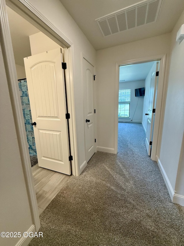 corridor with light colored carpet, baseboards, and visible vents