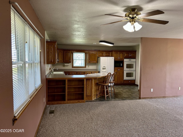 kitchen with white appliances, a peninsula, a ceiling fan, a sink, and baseboards