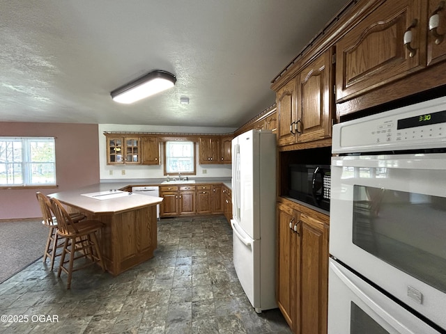 kitchen with white appliances, glass insert cabinets, a breakfast bar, a sink, and brown cabinets