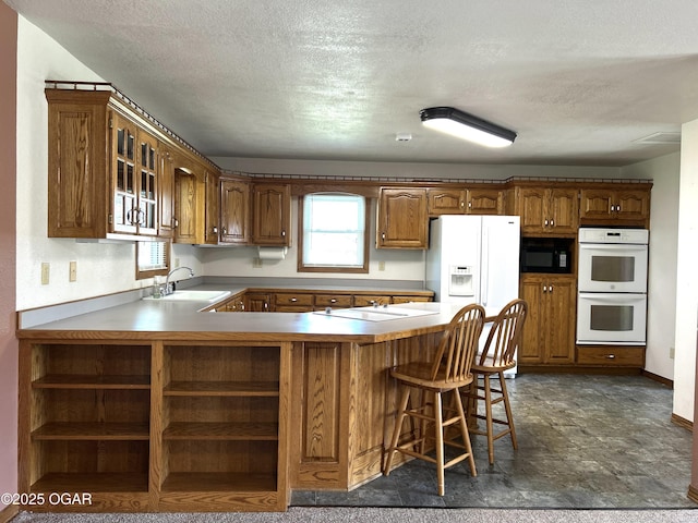 kitchen featuring a sink, white appliances, a peninsula, a textured ceiling, and brown cabinetry