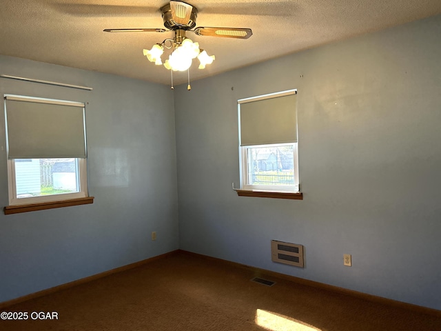 spare room featuring visible vents, a ceiling fan, heating unit, a textured ceiling, and carpet floors