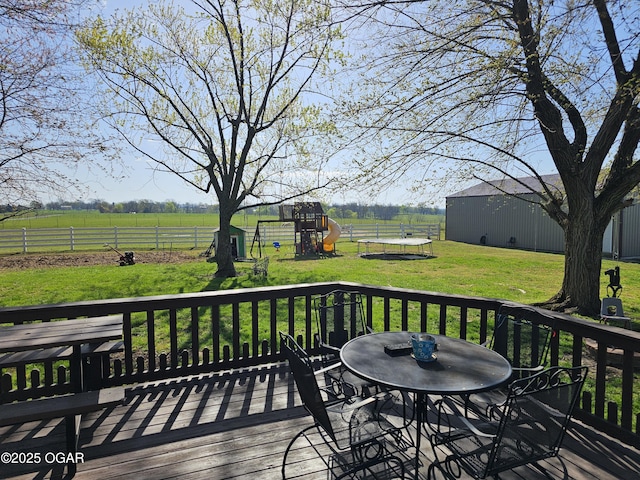 deck featuring a rural view, outdoor dining space, a playground, fence, and a yard