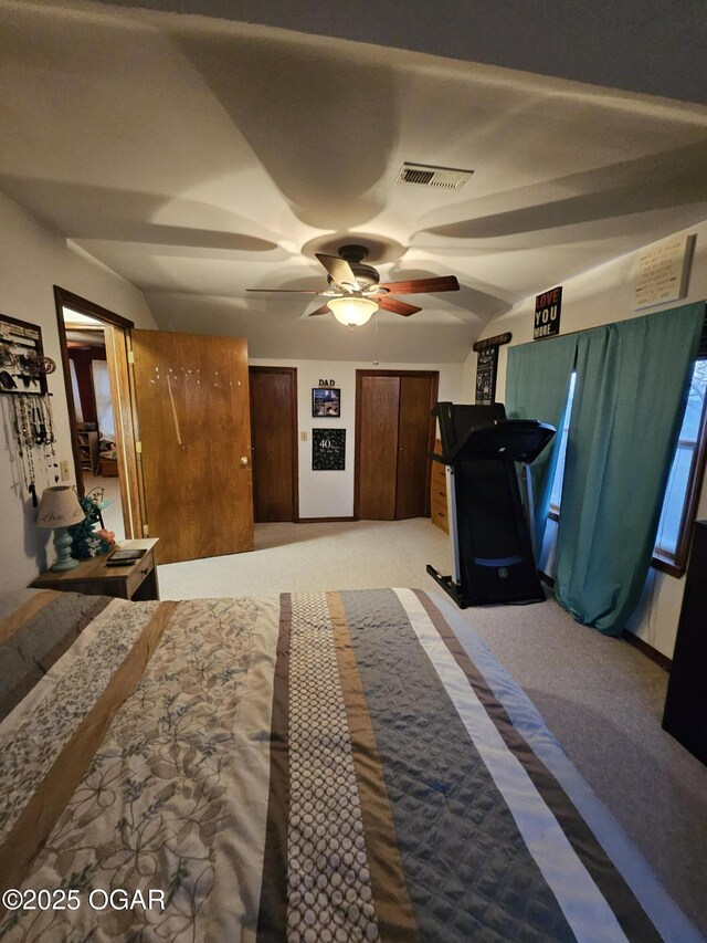 bedroom with light colored carpet, visible vents, vaulted ceiling, two closets, and a ceiling fan
