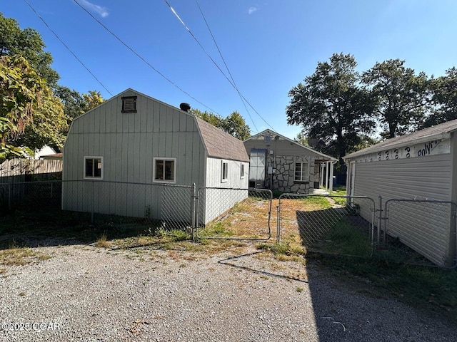 view of home's exterior with an outbuilding, a gambrel roof, fence, and a gate