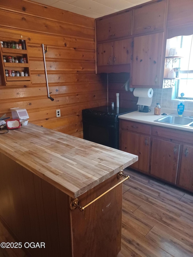 kitchen with butcher block counters, wood finished floors, a sink, black electric range oven, and wooden walls