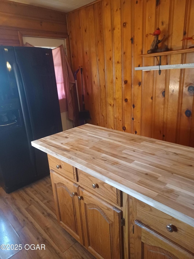 kitchen featuring wooden walls, black fridge, butcher block counters, brown cabinets, and wood finished floors