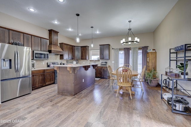 kitchen with tasteful backsplash, light countertops, premium range hood, stainless steel appliances, and a breakfast bar area