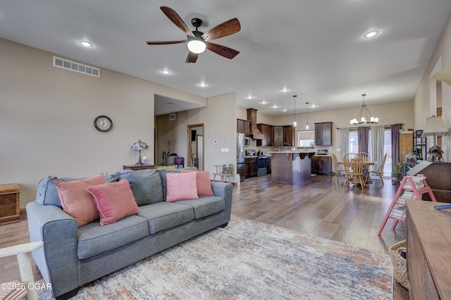 living room with visible vents, recessed lighting, wood finished floors, and ceiling fan with notable chandelier