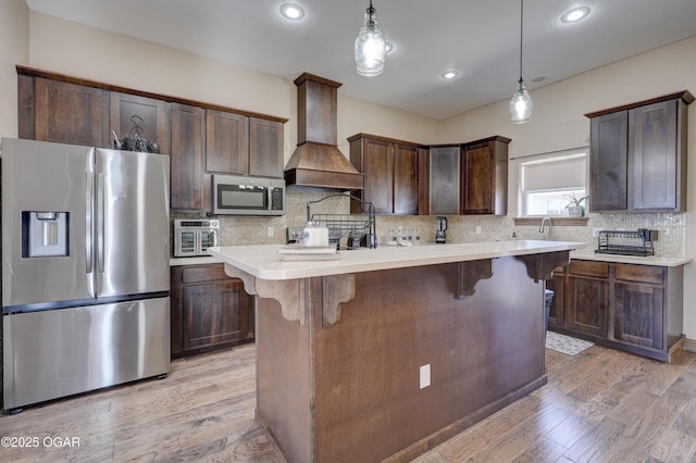 kitchen featuring custom exhaust hood, light wood-style flooring, dark brown cabinets, and appliances with stainless steel finishes