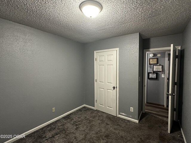 2027 P St SW, Miami, OK 74354 - unfurnished bedroom with a textured ceiling, dark colored carpet, and baseboards