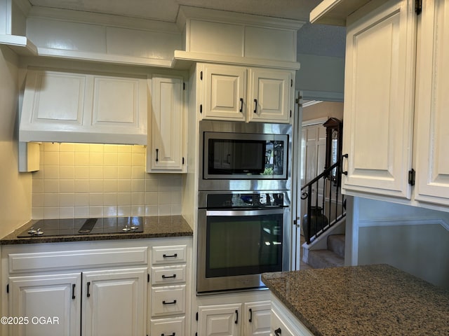 kitchen with white cabinets, appliances with stainless steel finishes, premium range hood, dark stone counters, and decorative backsplash