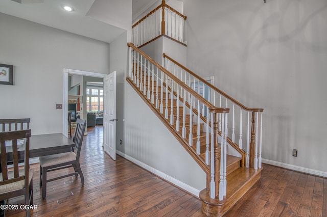 stairway with a towering ceiling, baseboards, recessed lighting, and wood-type flooring