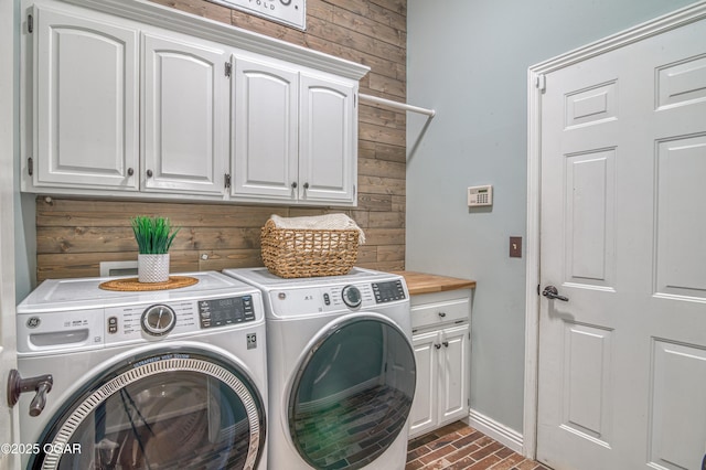 washroom with cabinet space, independent washer and dryer, wood walls, baseboards, and brick floor