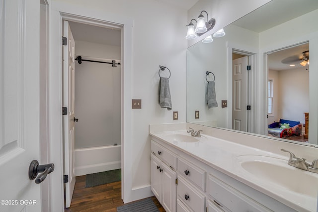 ensuite bathroom with double vanity, wood finished floors, bathtub / shower combination, and a sink