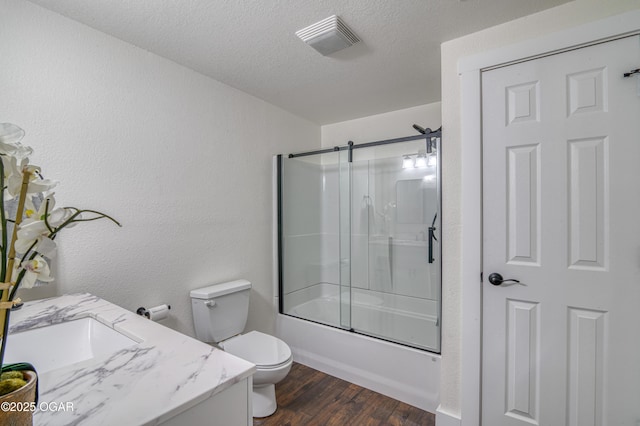 full bathroom featuring toilet, combined bath / shower with glass door, visible vents, a textured ceiling, and wood finished floors