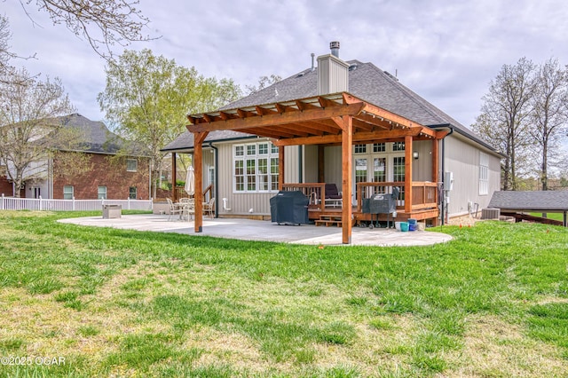 rear view of house featuring a deck, a lawn, roof with shingles, and a patio area