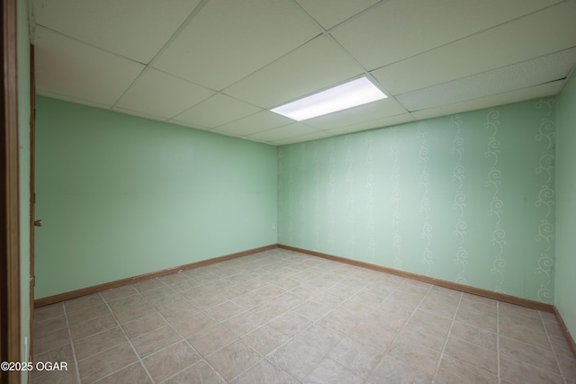 spare room with light floors, a paneled ceiling, and baseboards