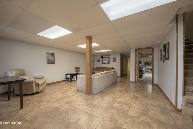 living area featuring baseboards, stairway, and a drop ceiling