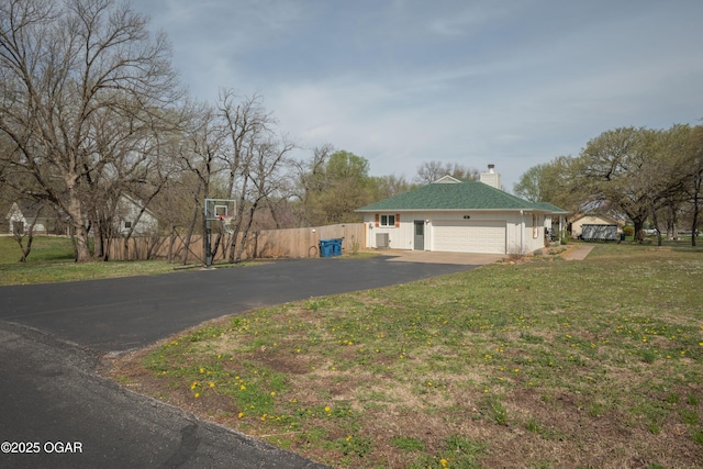 exterior space featuring a garage, a chimney, fence, aphalt driveway, and a front yard