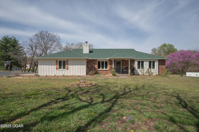 view of front of property featuring a chimney, covered porch, brick siding, and a front lawn