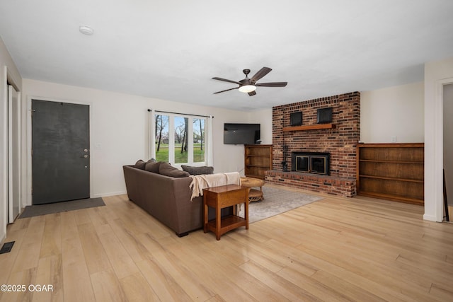 living area with visible vents, a fireplace, ceiling fan, baseboards, and light wood-style floors