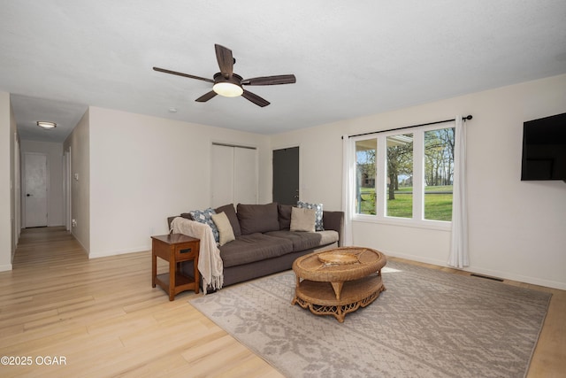 living room featuring light wood finished floors, visible vents, baseboards, and ceiling fan