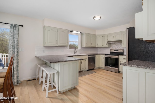 kitchen featuring a peninsula, a breakfast bar area, a sink, light wood-type flooring, and appliances with stainless steel finishes