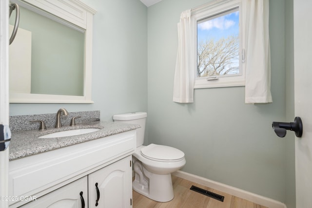 half bath featuring toilet, baseboards, visible vents, vanity, and wood finished floors