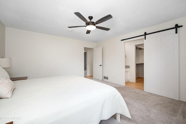 bedroom with visible vents, a barn door, baseboards, ceiling fan, and light colored carpet