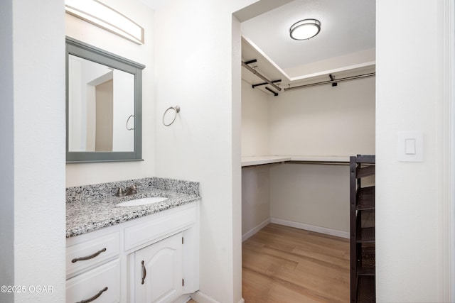 bathroom with baseboards, a spacious closet, vanity, and wood finished floors