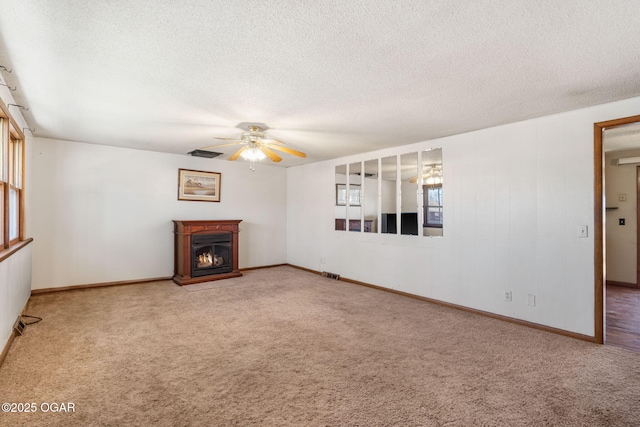 unfurnished living room featuring a textured ceiling, visible vents, a glass covered fireplace, carpet, and ceiling fan