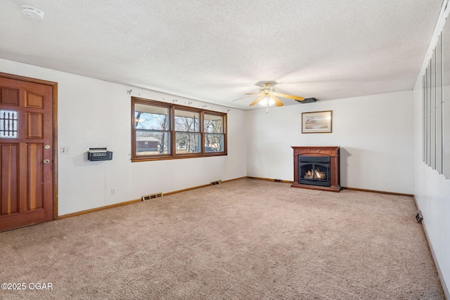 unfurnished living room featuring a textured ceiling, a warm lit fireplace, ceiling fan, carpet floors, and visible vents