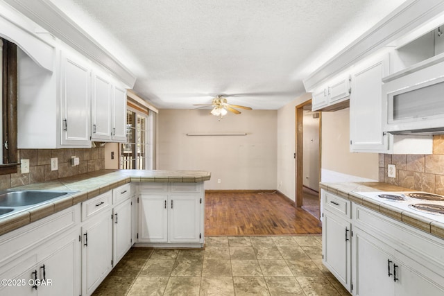 kitchen featuring tasteful backsplash, tile countertops, ceiling fan, a peninsula, and white cabinetry