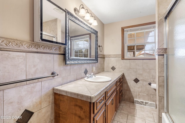 bathroom with tile patterned floors, a shower with shower door, tile walls, wainscoting, and vanity