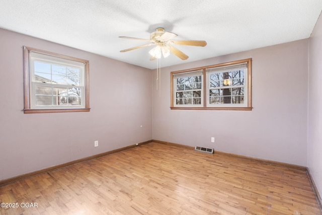 spare room with baseboards, a ceiling fan, light wood finished floors, and visible vents