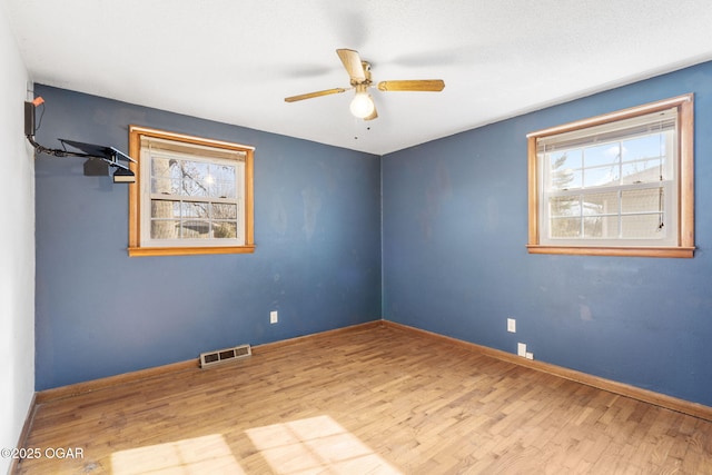 empty room featuring wood finished floors, a wealth of natural light, ceiling fan, and visible vents
