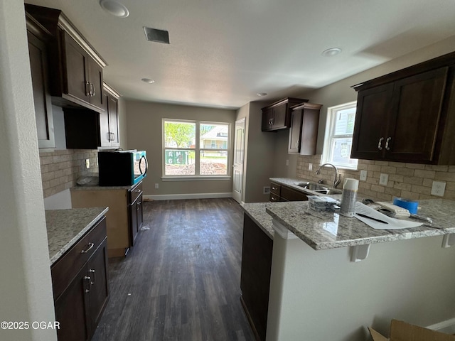 kitchen featuring stainless steel microwave, dark brown cabinetry, light stone countertops, and a sink
