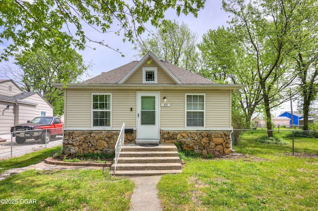 bungalow-style house with a shingled roof, fence, a front yard, and stone siding
