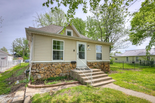bungalow-style house with roof with shingles, fence, stone siding, and a front lawn