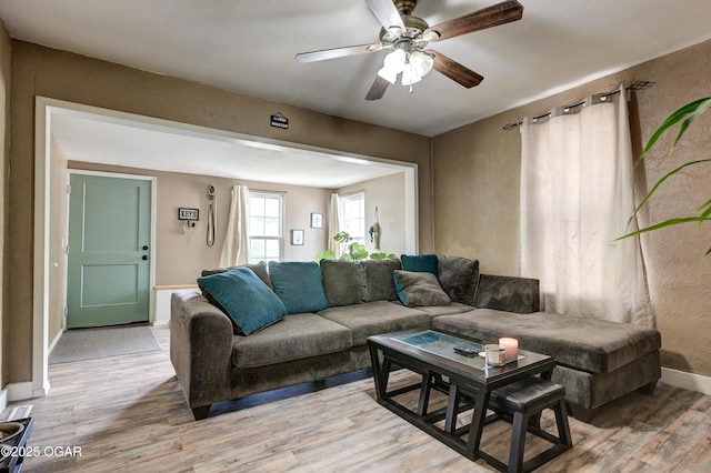 living room featuring a ceiling fan, baseboards, and light wood-style floors