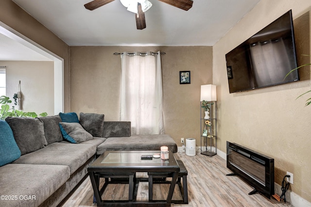 living room featuring ceiling fan, a textured wall, baseboards, and light wood-style floors