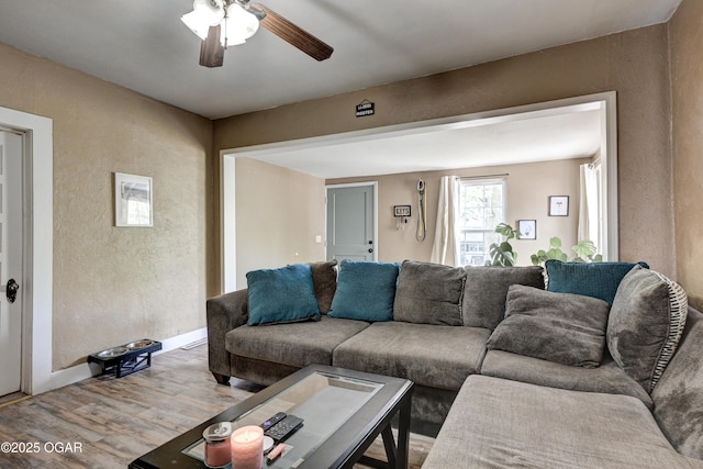 living room with baseboards, a textured wall, a ceiling fan, and light wood-type flooring