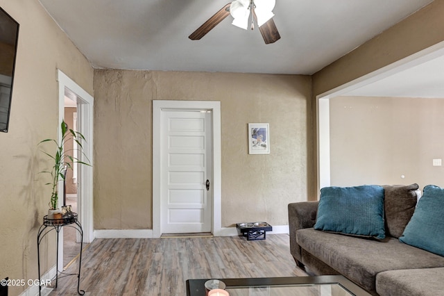 living area with baseboards, a ceiling fan, and wood finished floors