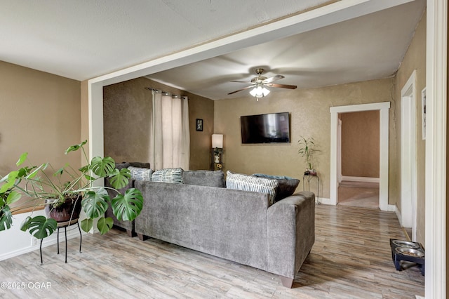 living room with a ceiling fan, baseboards, and light wood-type flooring