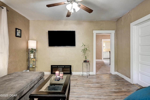 living room with baseboards, ceiling fan, a textured wall, and wood finished floors