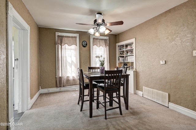 carpeted dining area featuring ceiling fan, visible vents, a textured wall, and baseboards