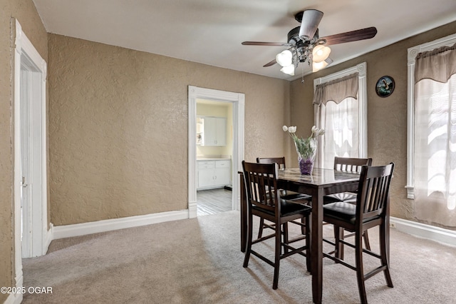 dining area featuring a textured wall, light carpet, and a ceiling fan