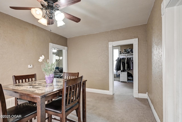 dining room featuring baseboards, a textured wall, ceiling fan, and light colored carpet